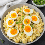 Overhead view of creamy deviled egg pasta salad topped with sliced boiled eggs and garnished with paprika and fresh green onions, showcasing a colorful, appetizing cold salad perfect for summer gatherings.