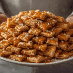 Alt Text: Golden salted caramel cracker bites piled on a vintage enamel plate, highlighting the buttery caramel and crispy oyster crackers with salt flakes.