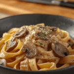 Alt Text: Steaming bowl of Italian pasta coated in a white Gorgonzola Truffle Cream Sauce with Mushroom and garnished with cracked black pepper.