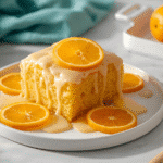 Overhead view of glazed Orange Bars in a baking pan surrounded by fresh Navel oranges and zest.