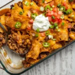 A scoop of Walking Taco Casserole being served on a white plate, showing layers of juicy beef, melted cheese, and tortilla chips.