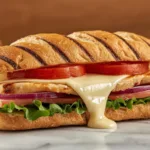 A side profile of a stacked Grilled Chicken Cordon Bleu Sandwich showing the texture of the grilled chicken and golden brioche.