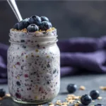 Person holding a spoon in a jar of Blueberry Overnight Oats With Yogurt and almond slices