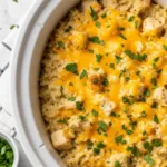A close-up of a creamy and cheesy slow cooker chicken and rice casserole dinner garnished with parsley in a white bowl.