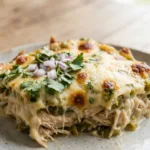 A spatula lifting a creamy serving of green chile chicken casserole with cheese pulling.