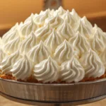 A bowl of glossy white italian meringue buttercream on a stand mixer.