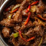 Crispy Beijing Beef Stir-Fry with red peppers and onions in a black wok.