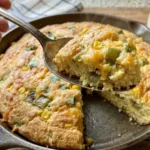 A whole Chiles Rellenos Cornbread in a cast iron skillet, golden crust showing green chiles and melted cheese.