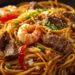 A close-up shot of Steak and Shrimp Lo Mein with broccoli and carrots in a black wok.