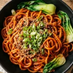 Close-up of glossy Gochujang Noodles in a black bowl with green onions.